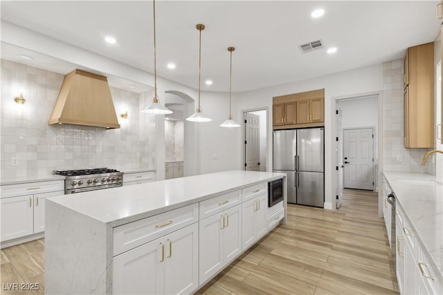 kitchen featuring appliances with stainless steel finishes, a center island, white cabinetry, custom range hood, and decorative light fixtures