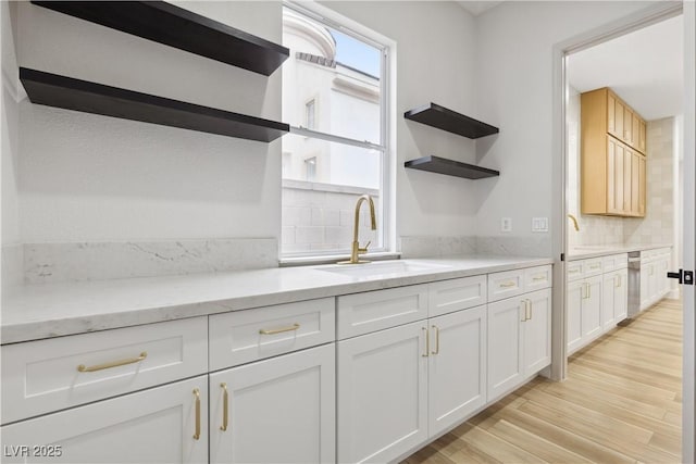 kitchen featuring white cabinetry, light wood-type flooring, sink, tasteful backsplash, and light stone counters