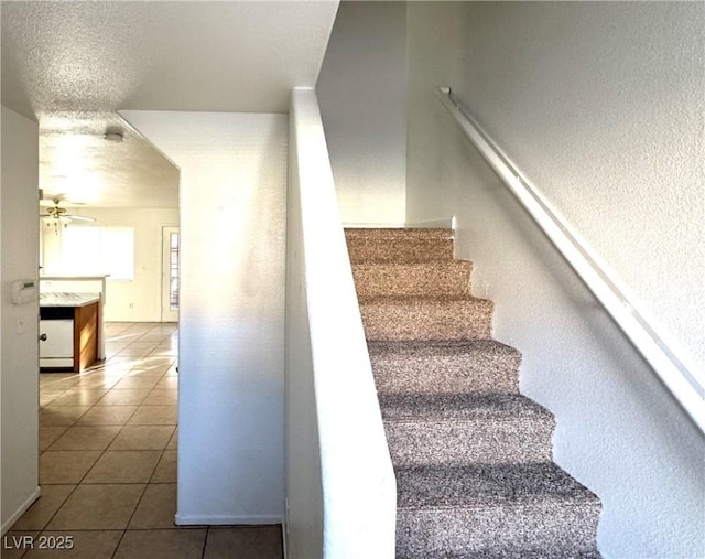 staircase featuring a textured ceiling, tile patterned flooring, and ceiling fan