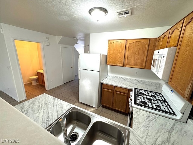 kitchen featuring sink, white appliances, a textured ceiling, and light tile patterned floors