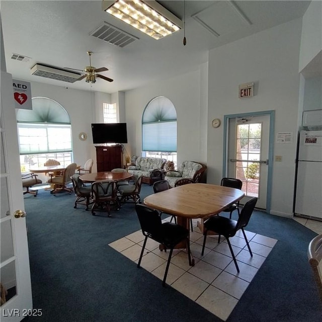 carpeted dining space with ceiling fan, a towering ceiling, and a wealth of natural light