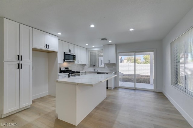 kitchen featuring light stone counters, a kitchen island, white cabinets, and appliances with stainless steel finishes