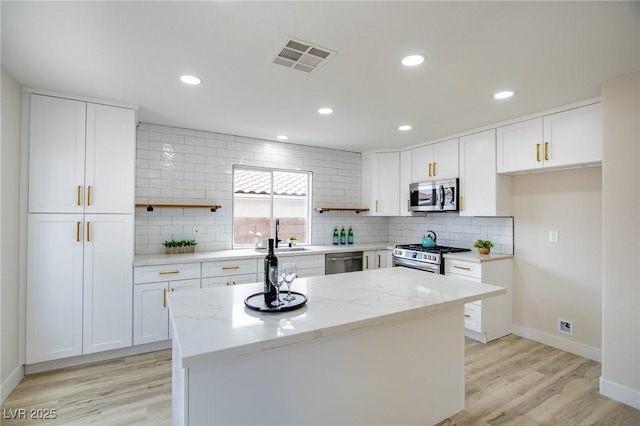 kitchen featuring white cabinetry, stainless steel appliances, a center island, light stone counters, and light hardwood / wood-style floors