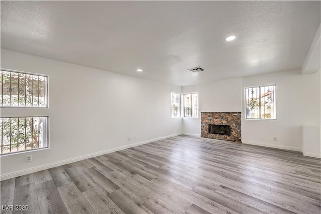 unfurnished living room featuring a stone fireplace, a textured ceiling, and light hardwood / wood-style flooring