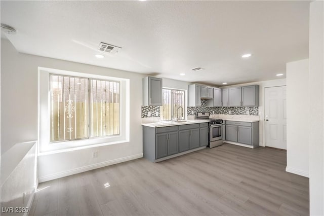 kitchen with tasteful backsplash, sink, gray cabinetry, stainless steel range oven, and light wood-type flooring