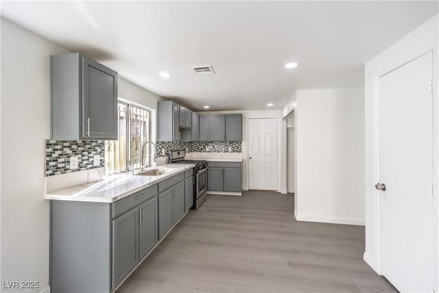 kitchen with sink, gray cabinetry, backsplash, gas stove, and light wood-type flooring