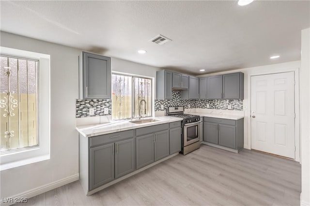 kitchen featuring sink, gray cabinetry, stainless steel gas range, and light wood-type flooring