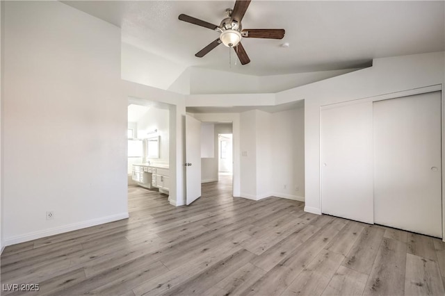 unfurnished bedroom with lofted ceiling, light hardwood / wood-style flooring, ceiling fan, ensuite bath, and a closet