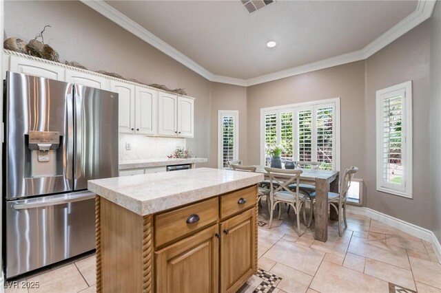 kitchen with crown molding, stainless steel fridge, white cabinetry, a kitchen island, and decorative backsplash