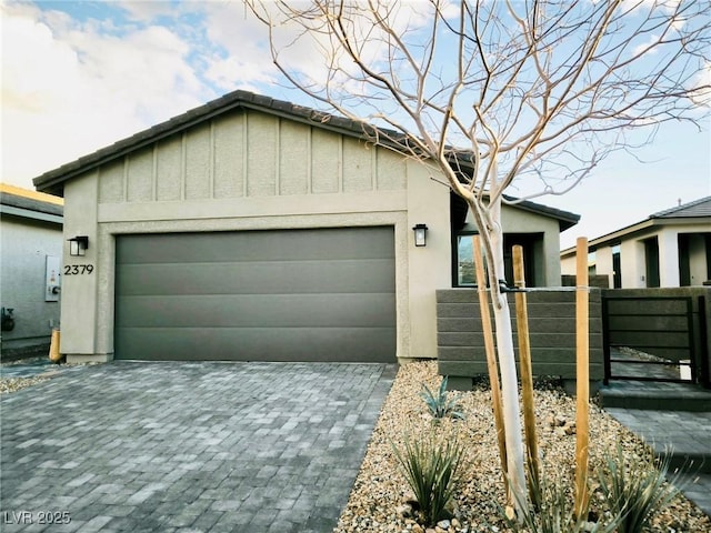 view of front of home featuring an attached garage, a gate, fence, decorative driveway, and stucco siding