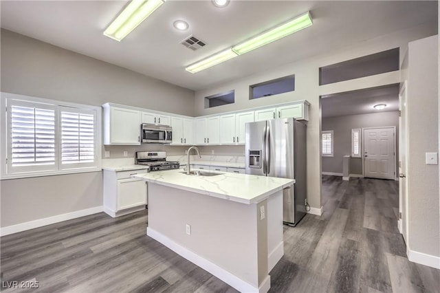 kitchen with appliances with stainless steel finishes, white cabinetry, an island with sink, sink, and light stone counters