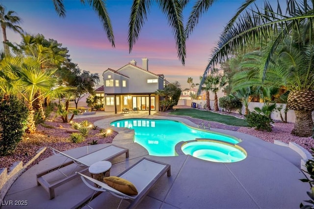 pool at dusk with an in ground hot tub and a patio