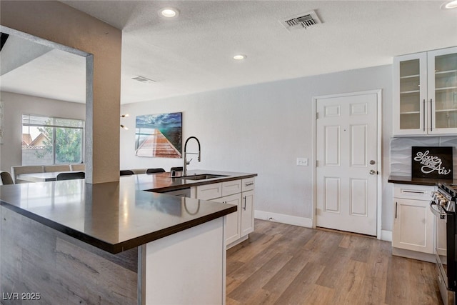 kitchen with sink, white cabinets, a kitchen breakfast bar, light hardwood / wood-style floors, and stainless steel range oven