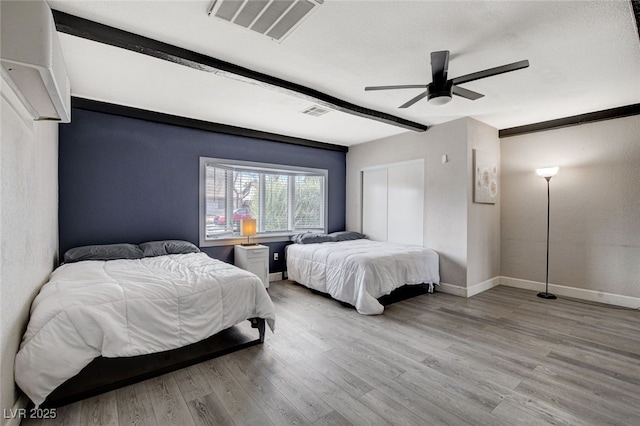 bedroom featuring beam ceiling, light hardwood / wood-style flooring, a textured ceiling, and ceiling fan