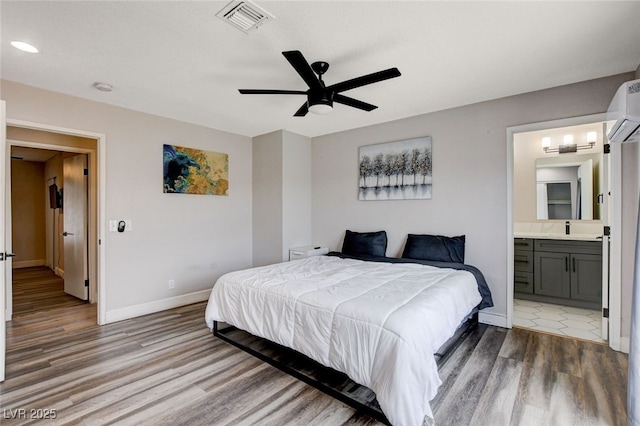 bedroom with hardwood / wood-style flooring, connected bathroom, a wall mounted AC, and ceiling fan