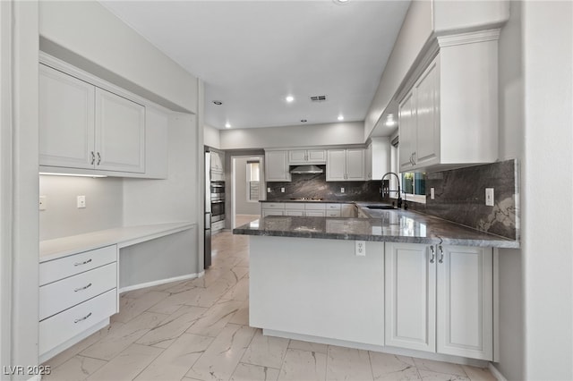 kitchen with sink, white cabinetry, backsplash, built in desk, and kitchen peninsula