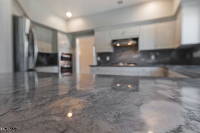 kitchen with dark stone counters, stainless steel fridge, exhaust hood, and white cabinets