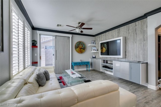 living area with a wealth of natural light, visible vents, wood finished floors, and ornamental molding