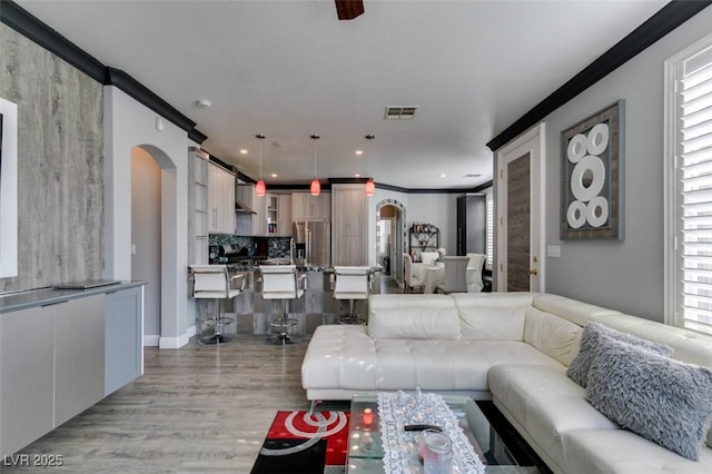 living room with light wood finished floors, visible vents, crown molding, recessed lighting, and arched walkways