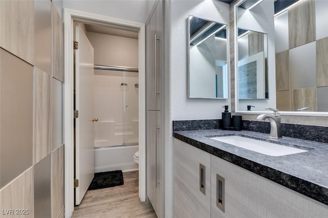 full bath with bath / shower combo with glass door, toilet, wood finished floors, and vanity