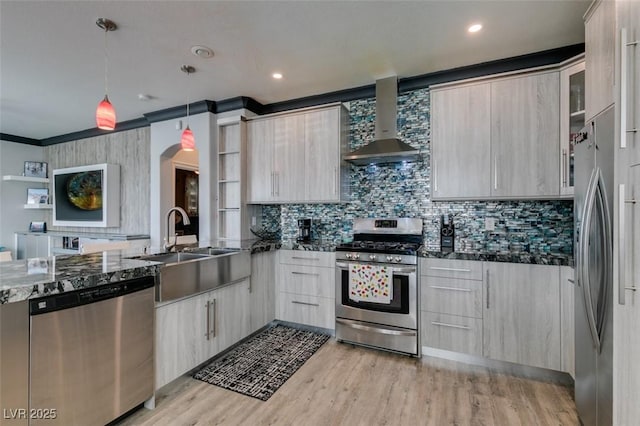 kitchen with arched walkways, a sink, stainless steel appliances, light wood-style floors, and wall chimney exhaust hood