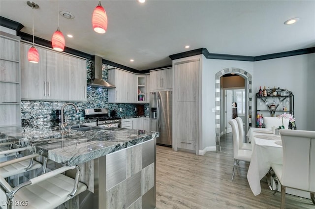 kitchen featuring a breakfast bar area, arched walkways, a sink, stainless steel appliances, and wall chimney range hood