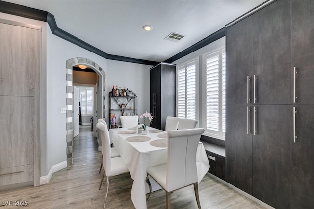 dining room with arched walkways, visible vents, light wood-style floors, and ornamental molding