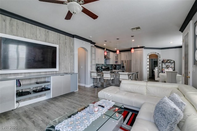 living area featuring visible vents, ornamental molding, wood finished floors, recessed lighting, and arched walkways