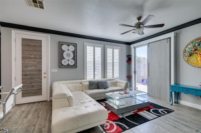 living area with visible vents, ornamental molding, a ceiling fan, wood finished floors, and baseboards