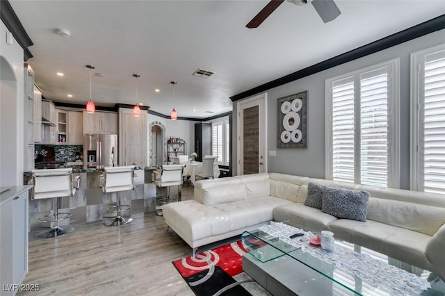 living room with a ceiling fan, visible vents, recessed lighting, ornamental molding, and light wood-style floors