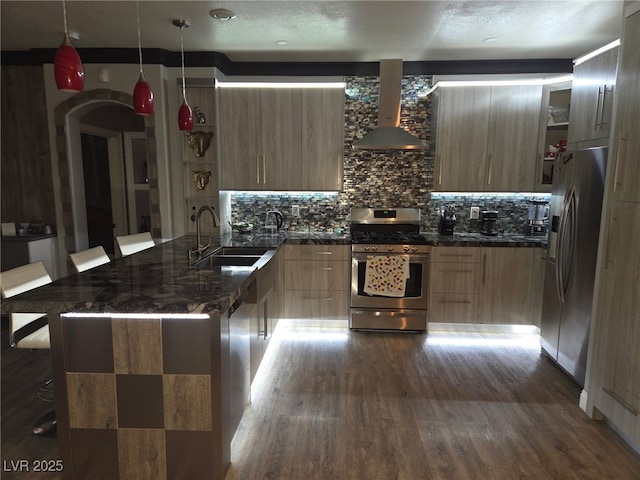 kitchen featuring a peninsula, a sink, appliances with stainless steel finishes, wall chimney range hood, and modern cabinets