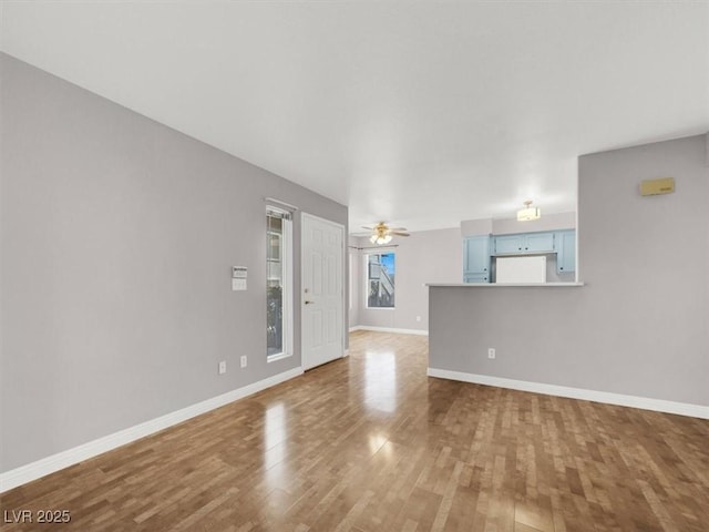 unfurnished living room featuring a ceiling fan, baseboards, and wood finished floors