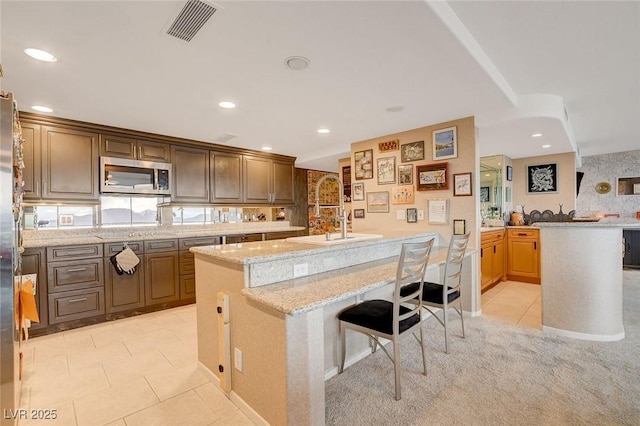 kitchen with light tile patterned flooring, sink, a kitchen bar, light stone countertops, and a center island with sink