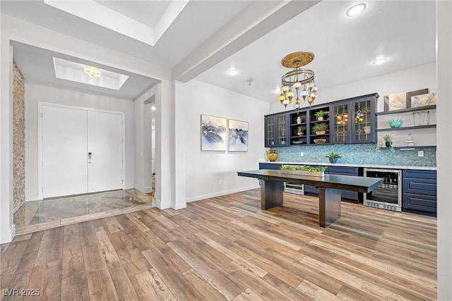 interior space with light wood-type flooring, wine cooler, decorative backsplash, hanging light fixtures, and an inviting chandelier