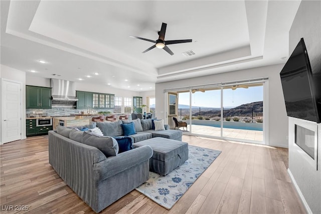 living room with a raised ceiling, ceiling fan, and light hardwood / wood-style flooring