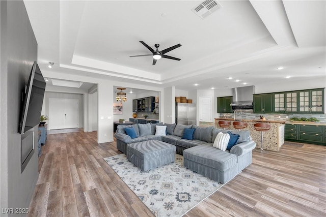 living room with a raised ceiling, ceiling fan, and light hardwood / wood-style floors