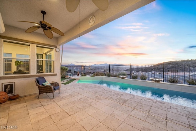 pool at dusk with a mountain view, a patio area, and ceiling fan