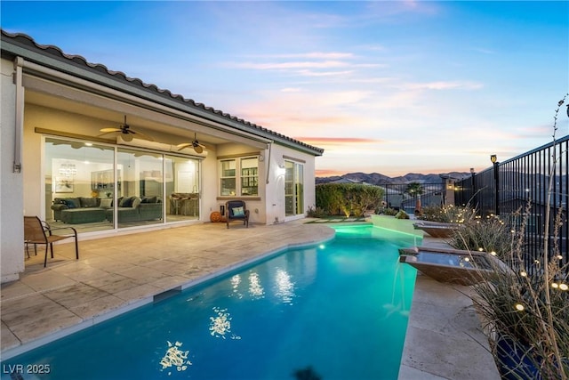 pool at dusk with a mountain view, a patio area, pool water feature, and ceiling fan