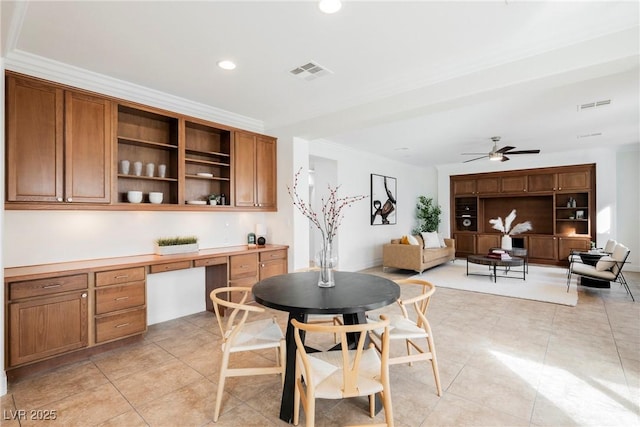 tiled dining space featuring ceiling fan, ornamental molding, and built in desk