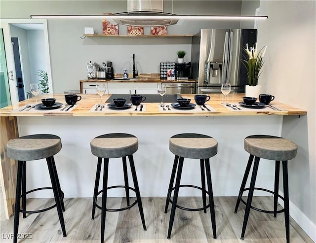 kitchen with light wood finished floors, wood counters, appliances with stainless steel finishes, a breakfast bar, and a sink