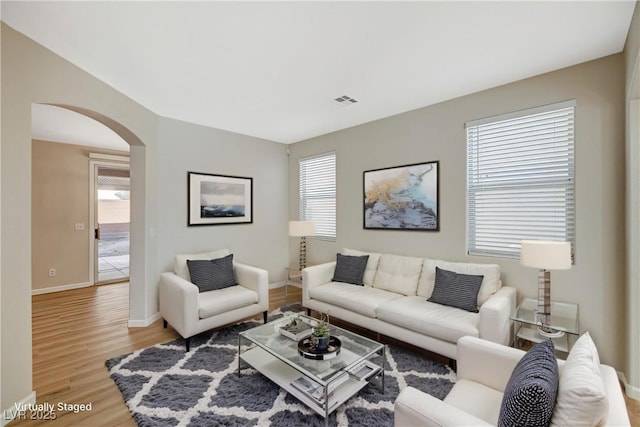 living area featuring light wood-type flooring, arched walkways, visible vents, and baseboards