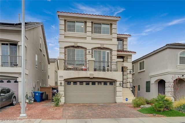 view of front of property featuring a tile roof, stucco siding, decorative driveway, a balcony, and a garage