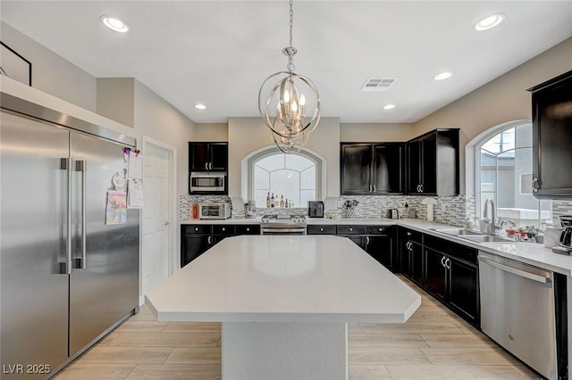 kitchen with visible vents, a center island, decorative backsplash, stainless steel appliances, and a sink