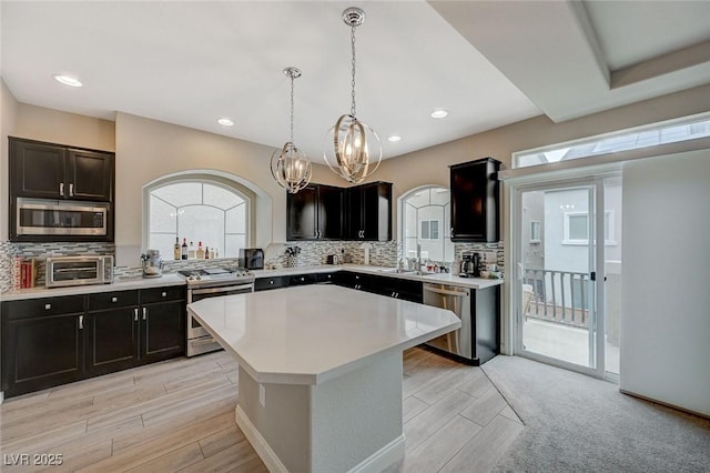 kitchen with light wood finished floors, backsplash, a kitchen island, light countertops, and appliances with stainless steel finishes