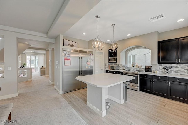 kitchen with visible vents, stainless steel appliances, decorative backsplash, light countertops, and dark cabinets