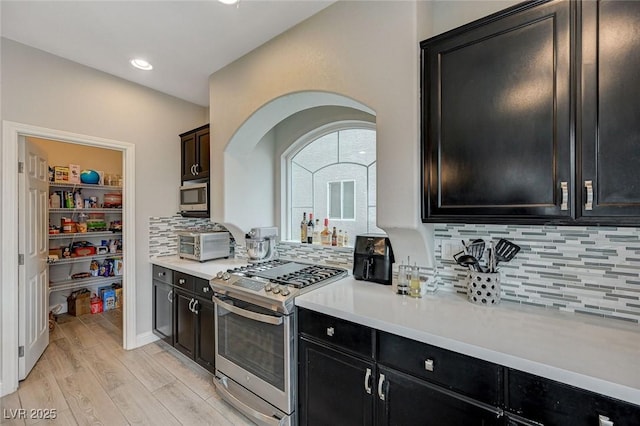 kitchen featuring decorative backsplash, light wood-style flooring, stainless steel appliances, and light countertops