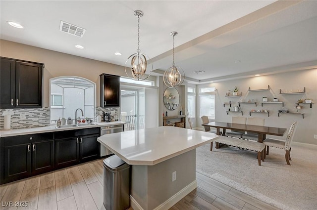 kitchen featuring visible vents, a kitchen island, a sink, light countertops, and tasteful backsplash