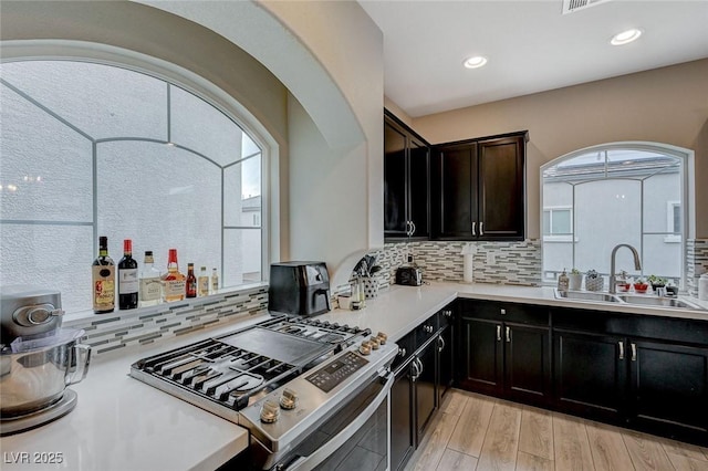 kitchen featuring light countertops, decorative backsplash, light wood-style flooring, gas stove, and a sink