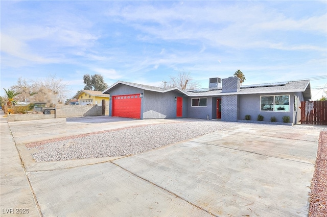 view of front facade featuring stucco siding, an attached garage, roof mounted solar panels, fence, and driveway