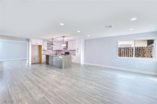 unfurnished living room with recessed lighting, visible vents, a sink, light wood-type flooring, and baseboards